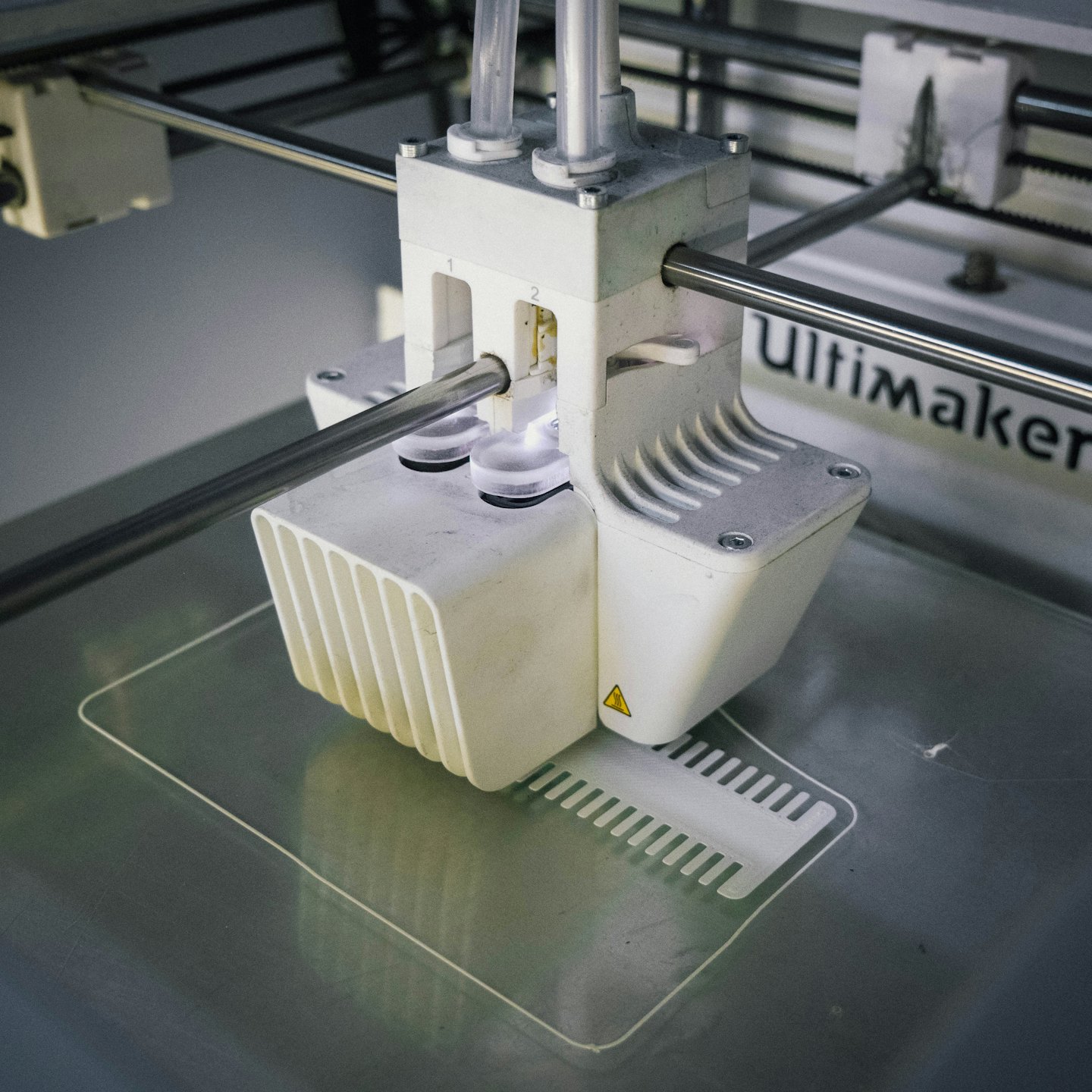 Imprimante 3D extrudant du filament blanc sur un plateau métallique.
