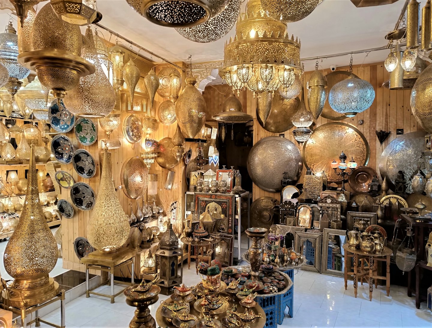 Des lampes et de la dinanderie ouvragées en laiton et argent remplissent une boutique.