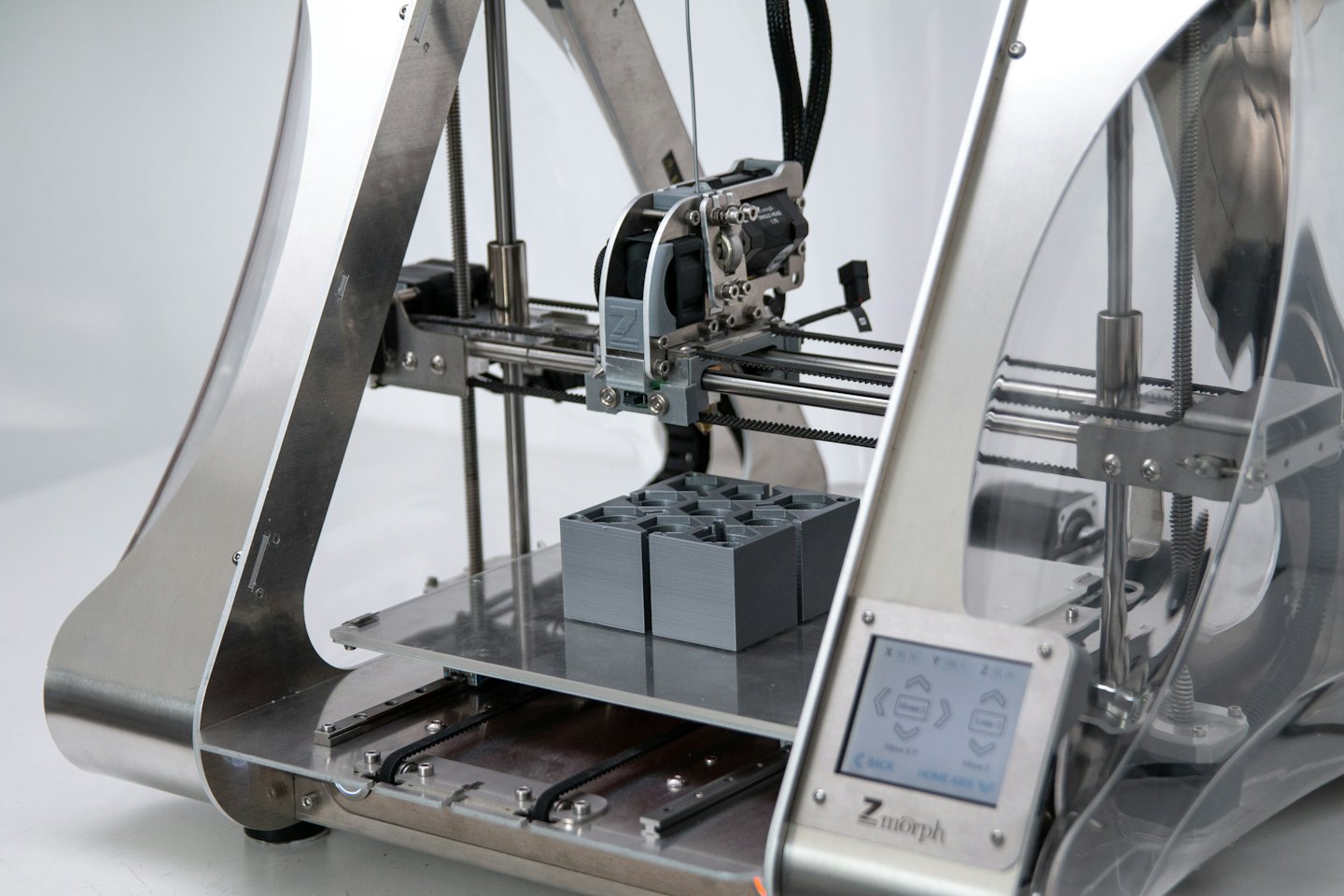 Une imprimante 3D créant des objets gris sur sa plateforme.