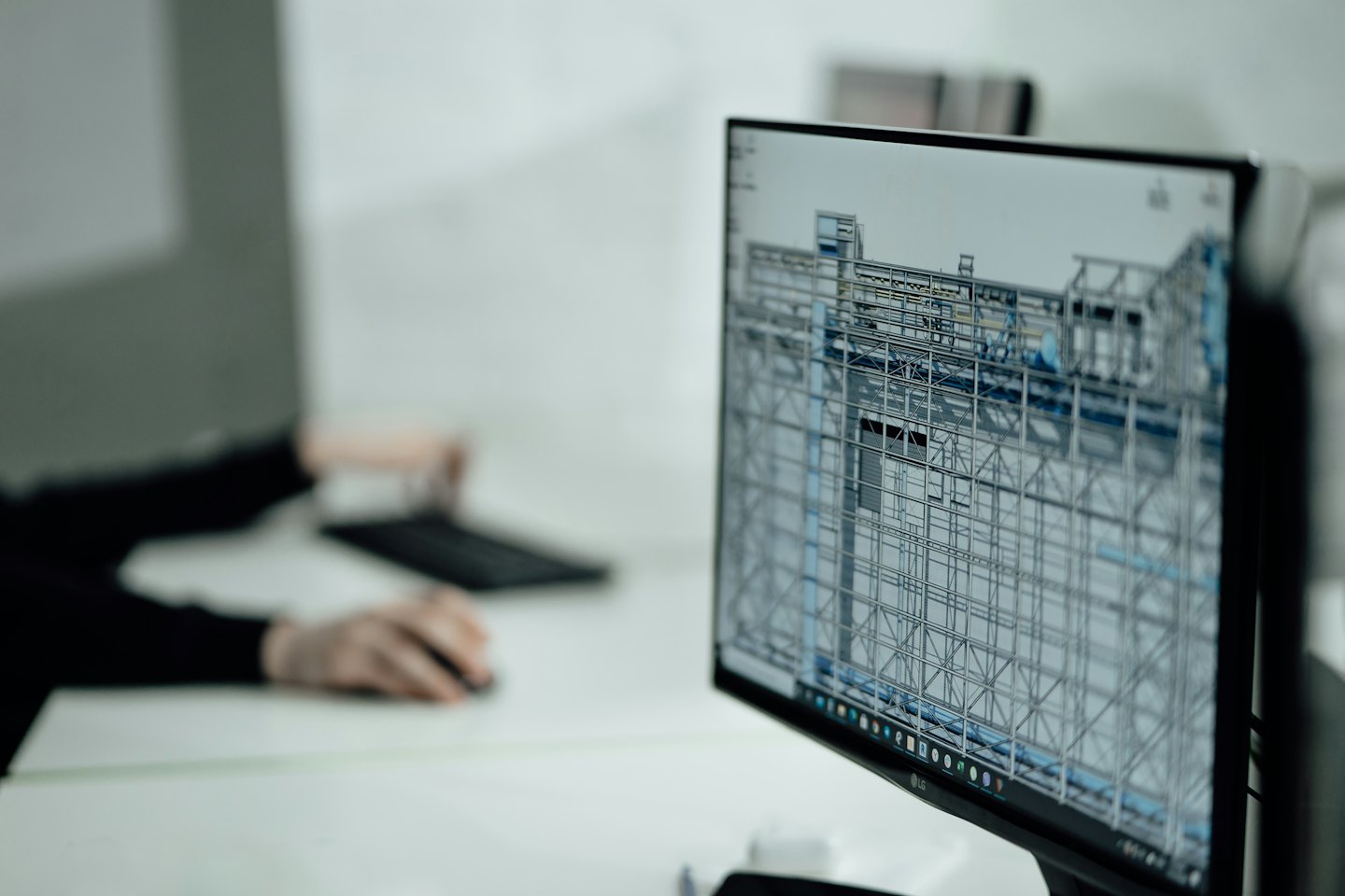 Un écran d'ordinateur affiche un modèle filaire 3D avec des mains sur le clavier.
