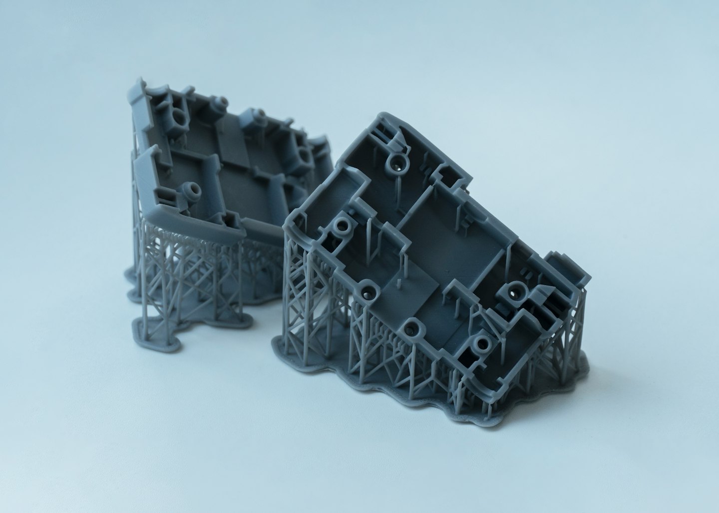 Deux prototypes en résine imprimés en 3D gris avec supports attachés.